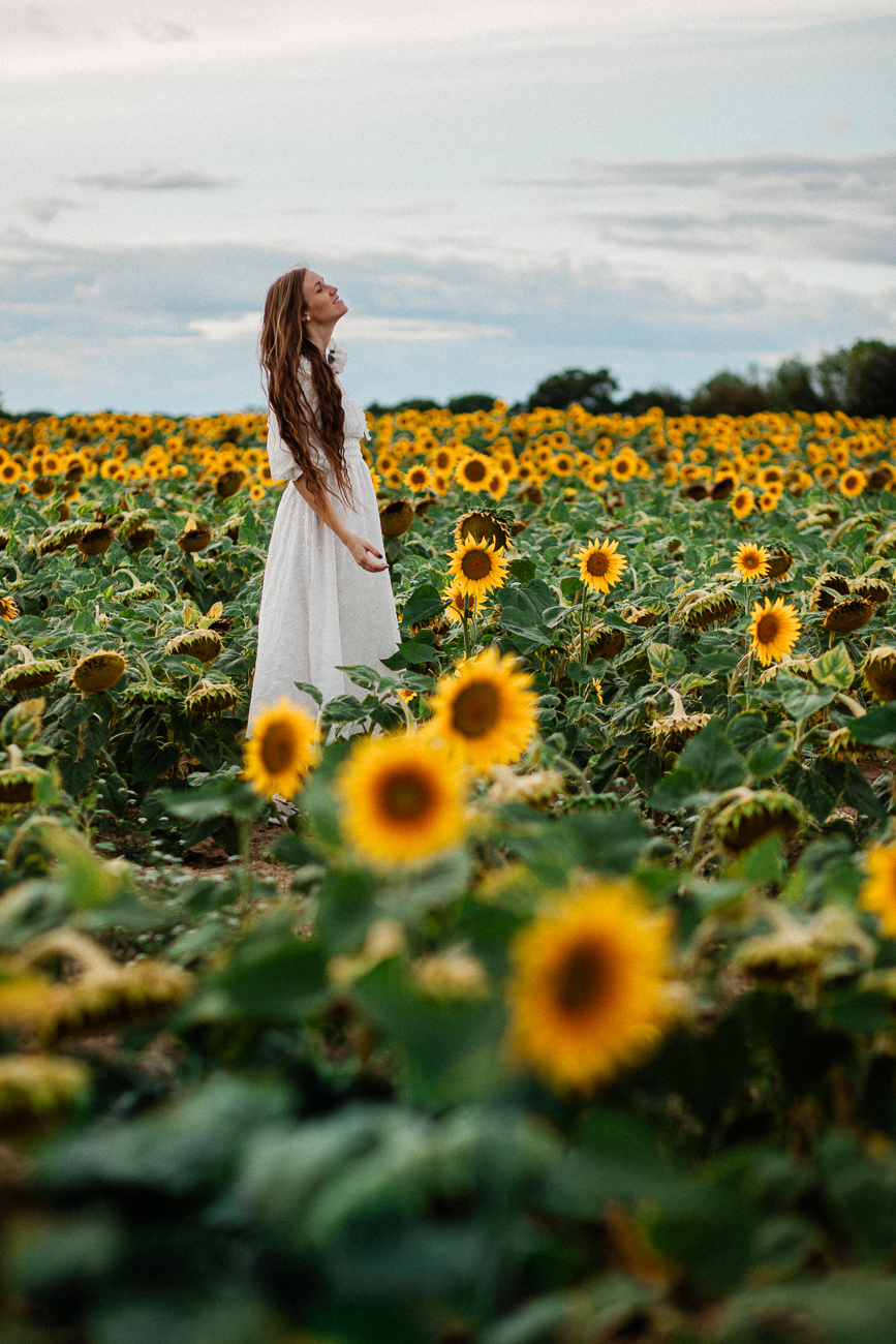a lady in white standing in a sunflower field