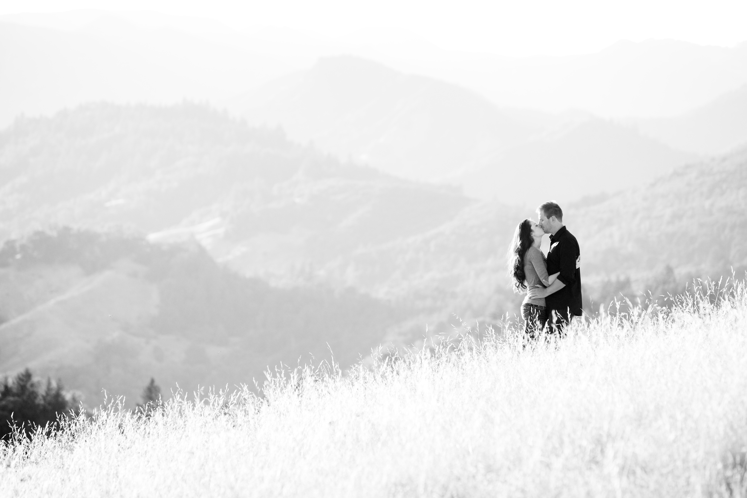a monochrome image of a couple kissing in a field